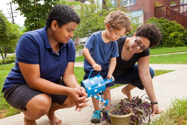 Parents helping their child playing with pottery in the garden.