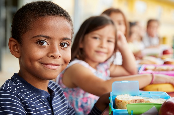 Children sitting on a classroom in front of a meal.