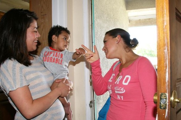 Home visitor greeting a mother with her baby, while entering a house.