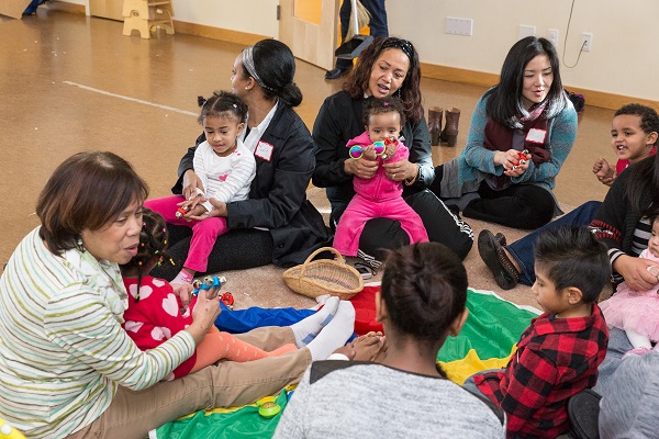 Parents, children, and home visitors sitting in the floor at a socialization meeting.