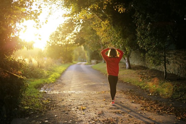 Mujer viendo el amanecer mientras camina por un camino rural