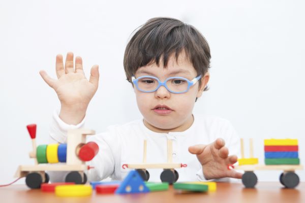 Niño con necesidades especiales usando anteojos y jugando con juguete de tren