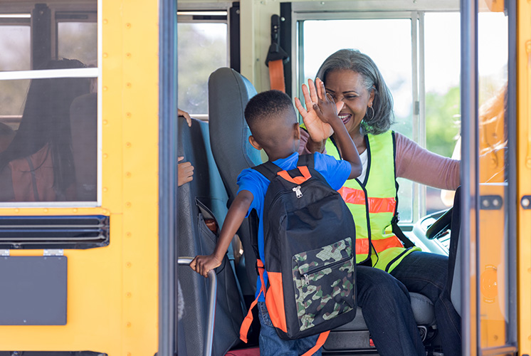 Child getting into the bus and greeted by the bus driver.