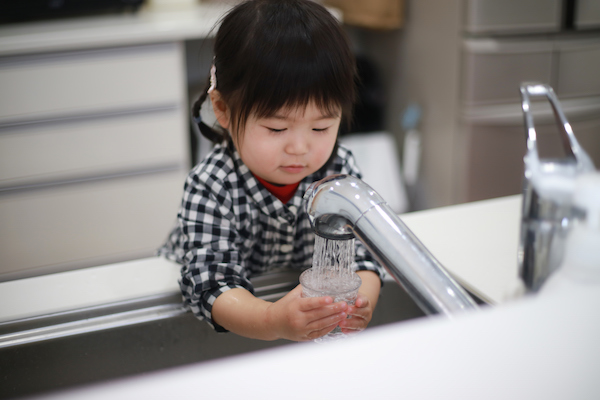 Child filling a glass with water from a faucet.