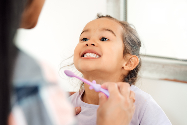 Child smiling while brushing her teeth.