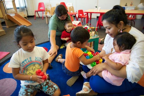 Teachers and toddlers sitting in a classroom.