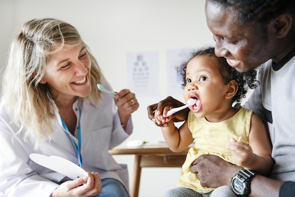 Dentista y padre mostrando a un niño cómo usar un cepillo de dientes.