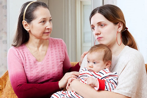 Woman talking with a mother holding a baby while not feeling well.