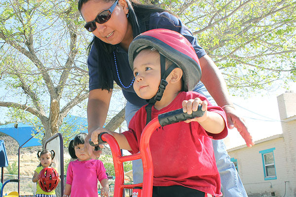 Teacher helping a child ride a tricycle.