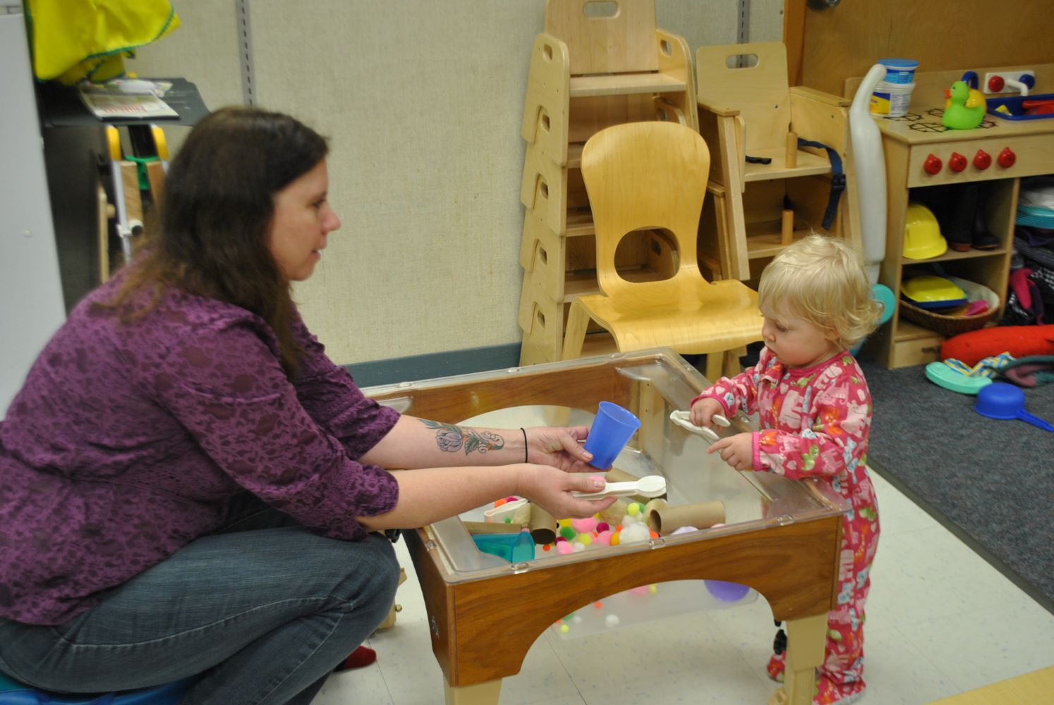 Adult showing a toddler different items at the sensory table.