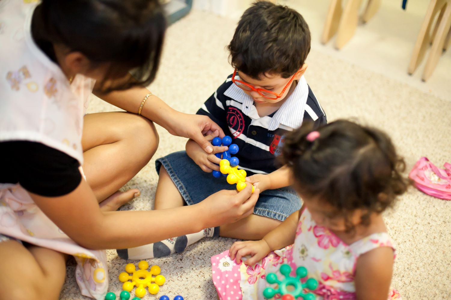 Young boy wearing glasses is shown how to use interlocking puzzle pieces.