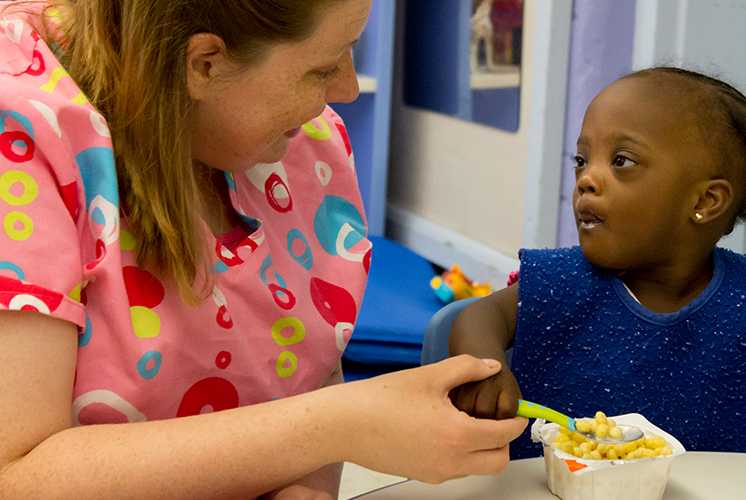 caregiver helps girl eat cereal