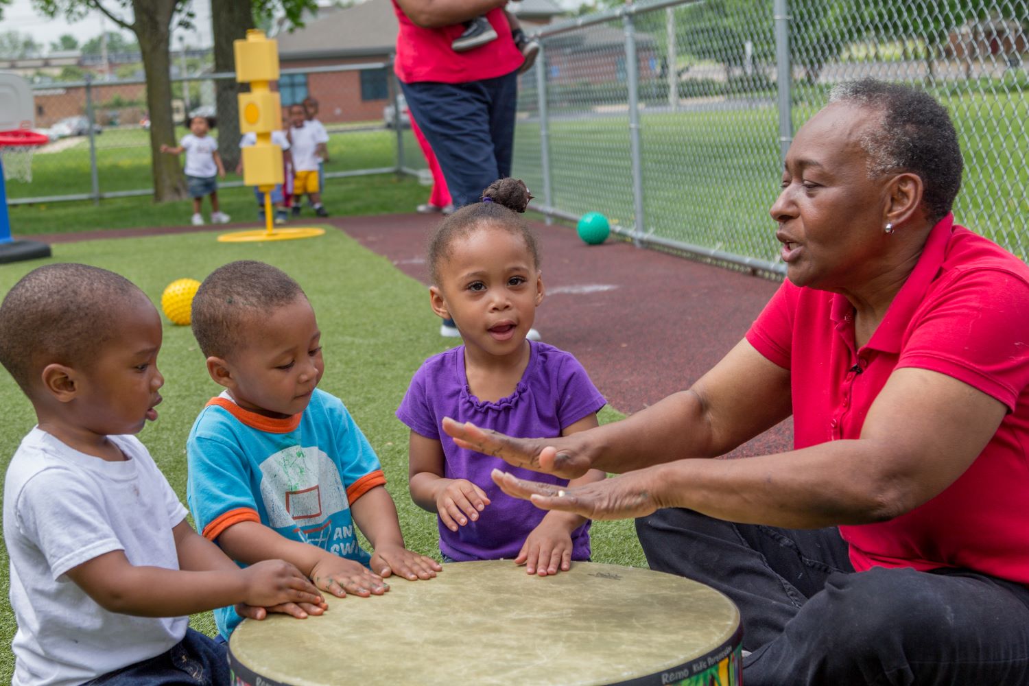 Chidren and adult drumming on a tabletop in a playground.