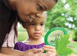 woman and child with magnifying glass looking at plant