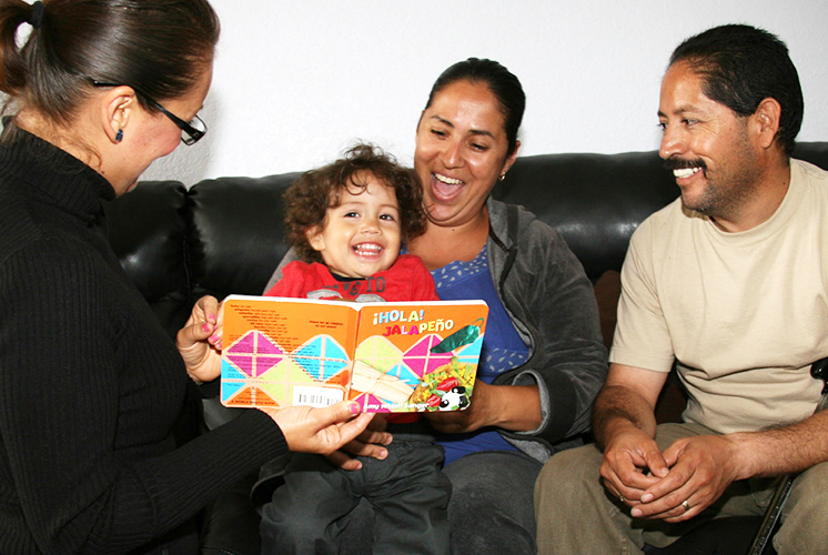 A home visitor reads a book with a family