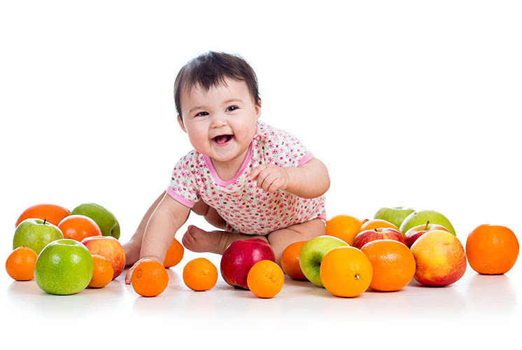 Un bebé riendo sentado en medio de muchas frutas