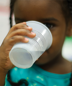 Niña bebiendo agua de una taza de plástico