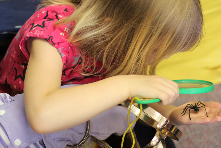 Girl looking at spider toy with magnifying glass