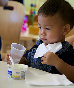 Niño pequeño comiendo yogur y bebiendo agua