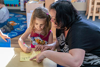 A teacher supervises a girl writing letters