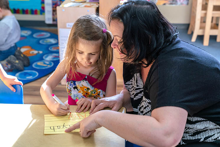 a teacher helps a girl printing letters