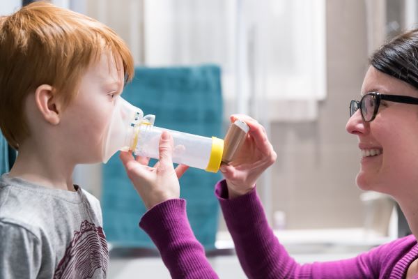 Adulto ayudando a un niño a usar un inhalador para el asma.