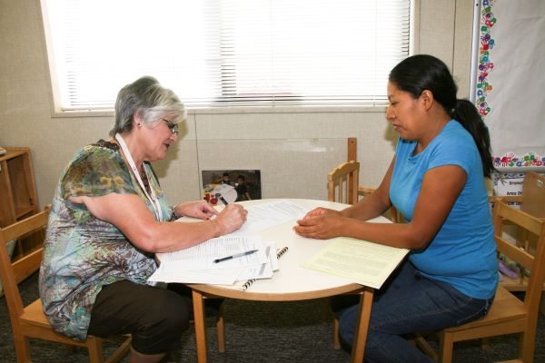 Two woman sitting at opposite ends of a table taking notes.