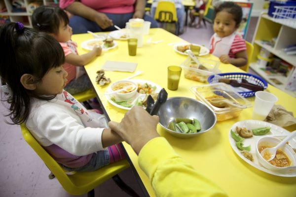 Punto de vista de un adulto entregando una pinza para ensalada a un niño para que pueda servirse a sí mismo.