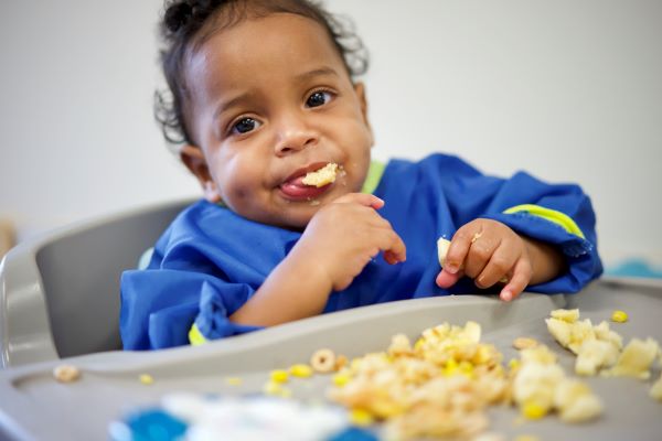 Un niño en una silla alta llevándose comida a la boca.