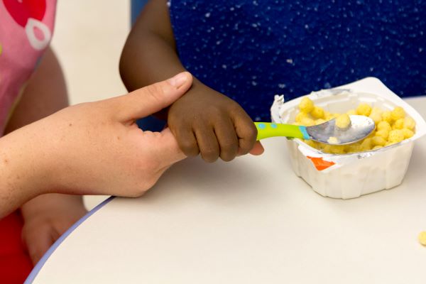 Un adulto que guía la mano de un niño mientras sostiene una cuchara.