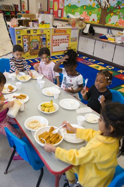 Un grupo de niños comiendo en una mesa larga.