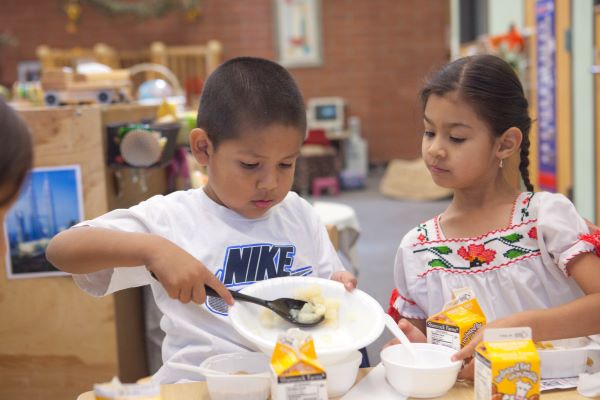 Un niño y una niña sirviéndose comida.