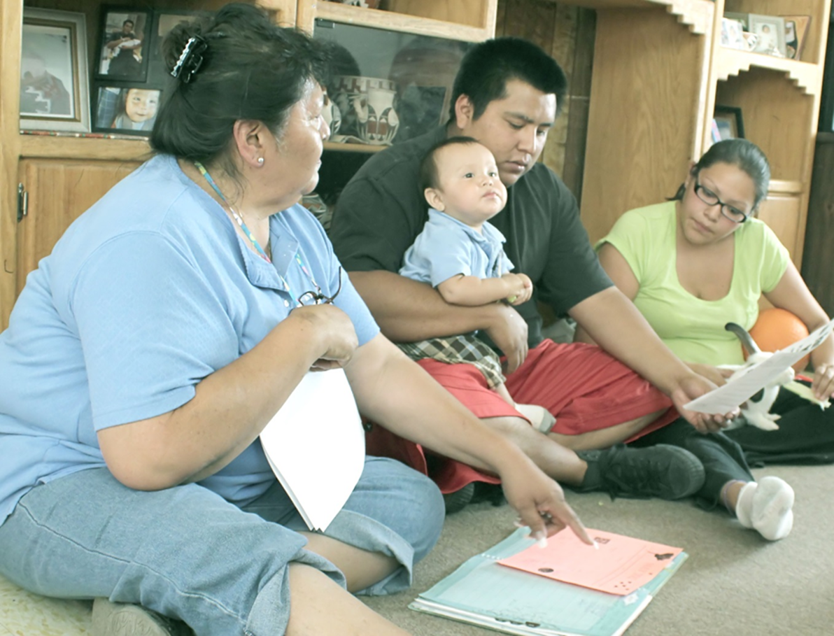 Home visitor jotting down notes while talking with parents and child.