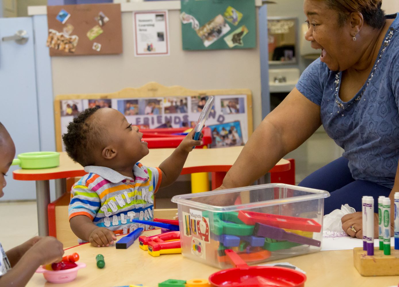 Smiling toddler shows teacher a magnifying glass.