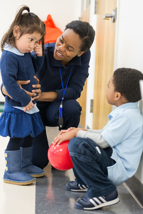 Instructor holding girl, and boy laying against a wall