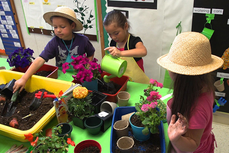 Los niños se reunieron alrededor de una mesa llena de plantas y herramientas de jardinería