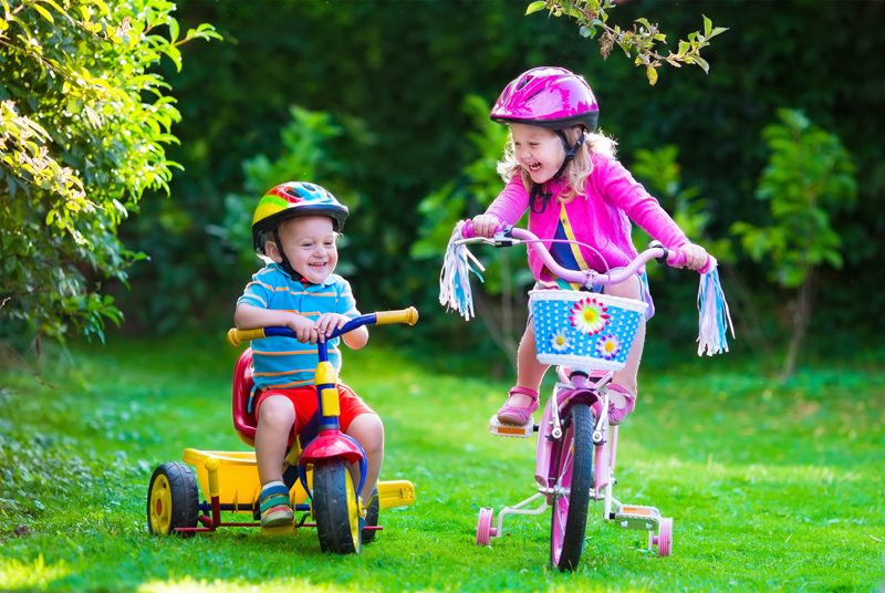 Children wearing helmets as they ride their bicycles outside.