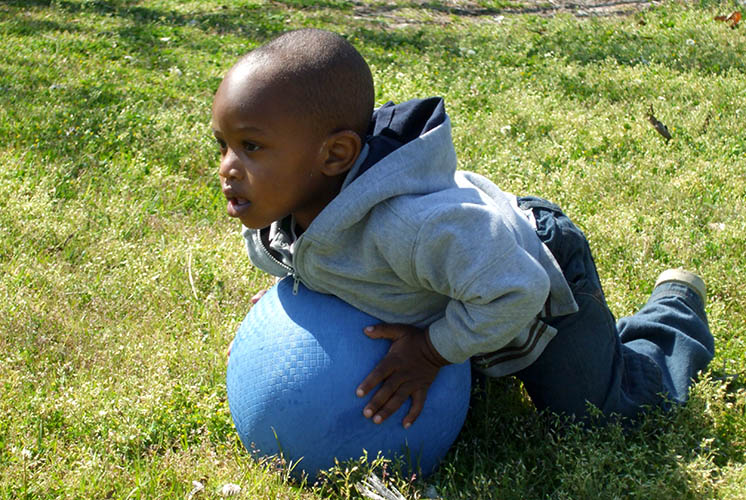 a boy lays on an inflatable ball on a grassy lawn