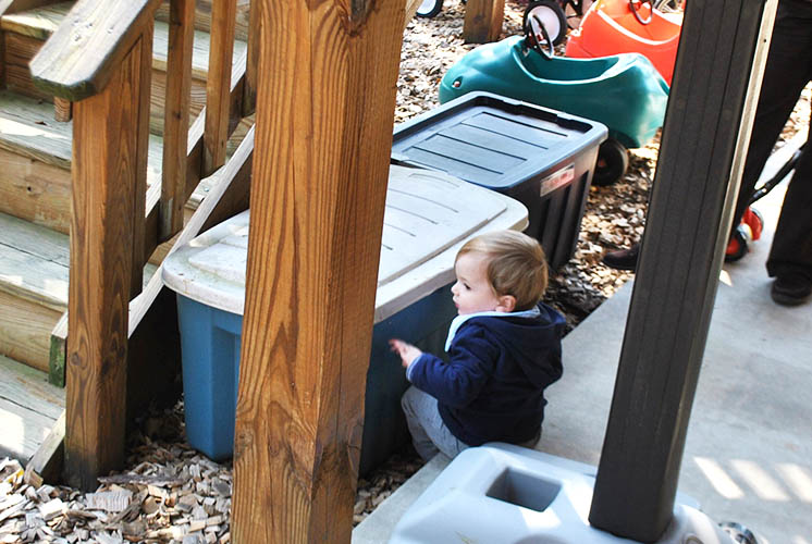 a boy sits outside next large plastic storage bins