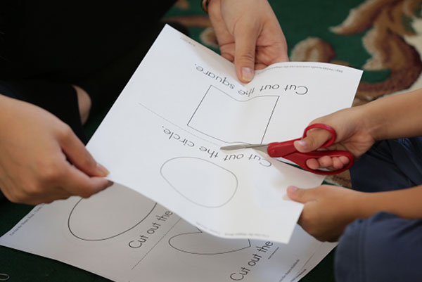 Teacher cutting paper with a child