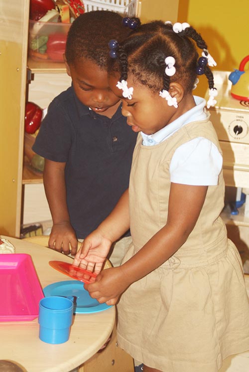 A girl and boy play with plastic dishes at a table