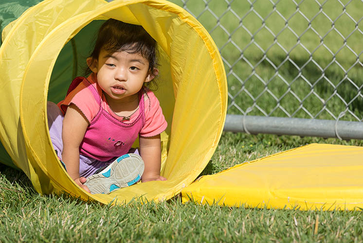 A girl crawls through a play tunnel in the grass