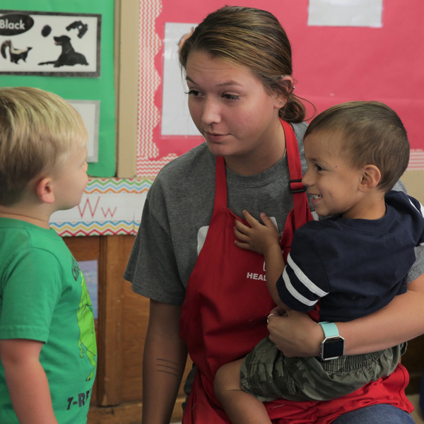 Maestra de Head Start cargando a un niño mientras habla con otro