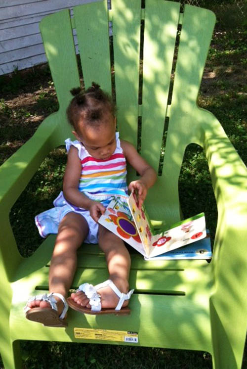 una niña sentada en una silla en la sombra mirando un libro