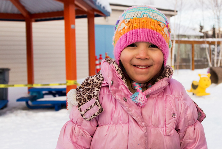 A smiling girl stands in a snow covered playground