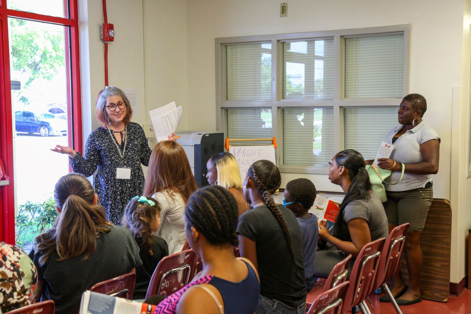 Staff members addressing parents and children at a meeting.