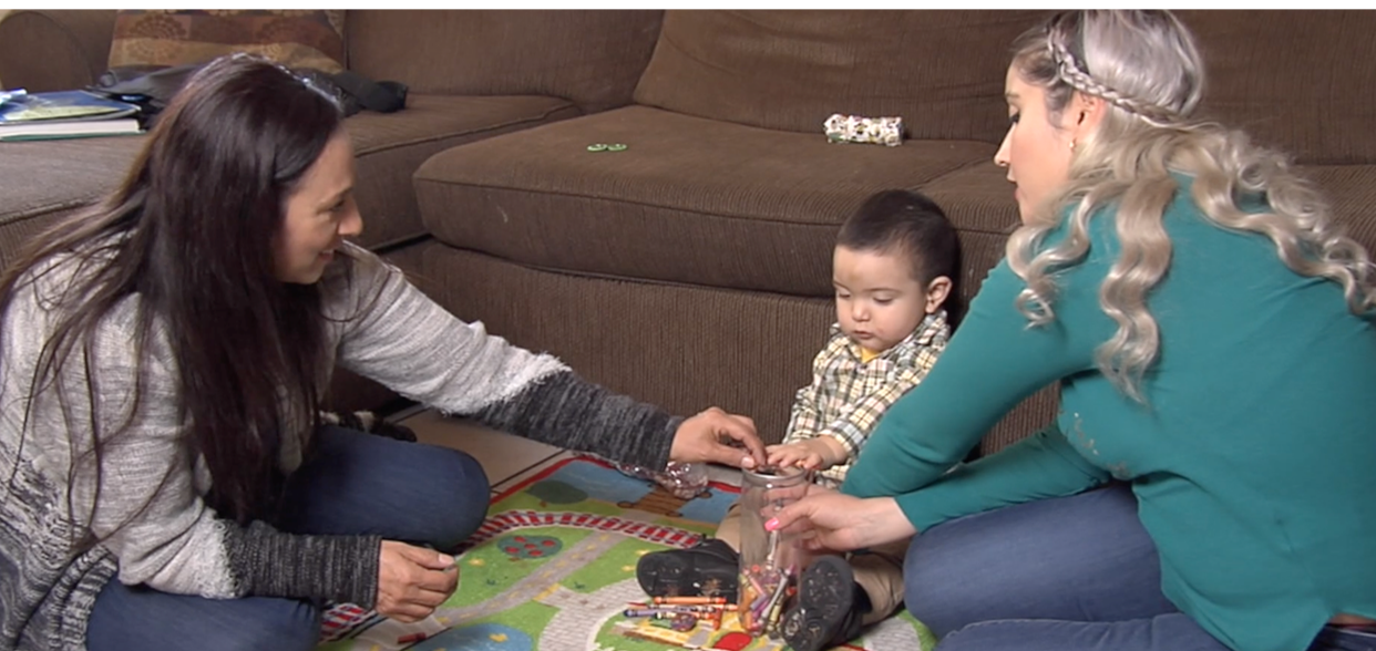 Two adults sitting on floor interacting with toddler.