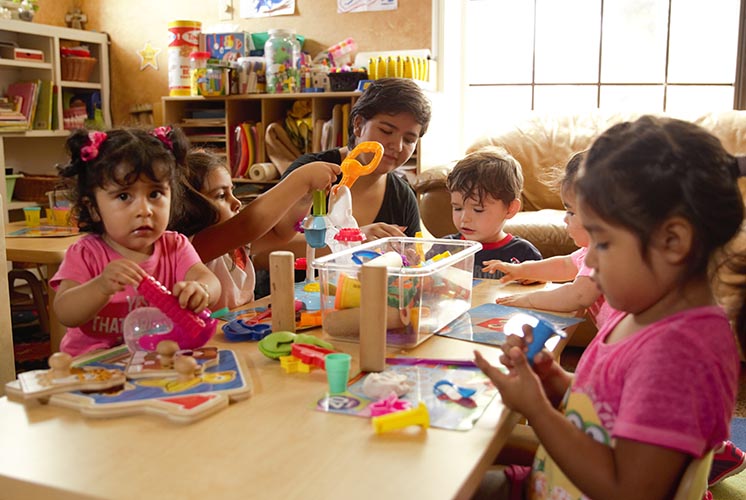 Children play with toys at a table while a teacher helps