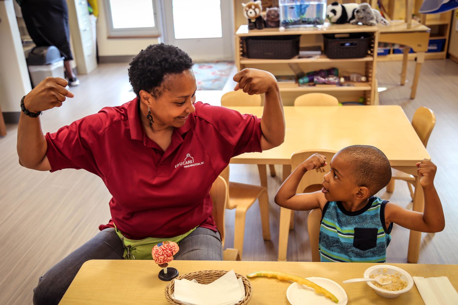 Maestra y niño levantando los brazos y mostrando los músculos.