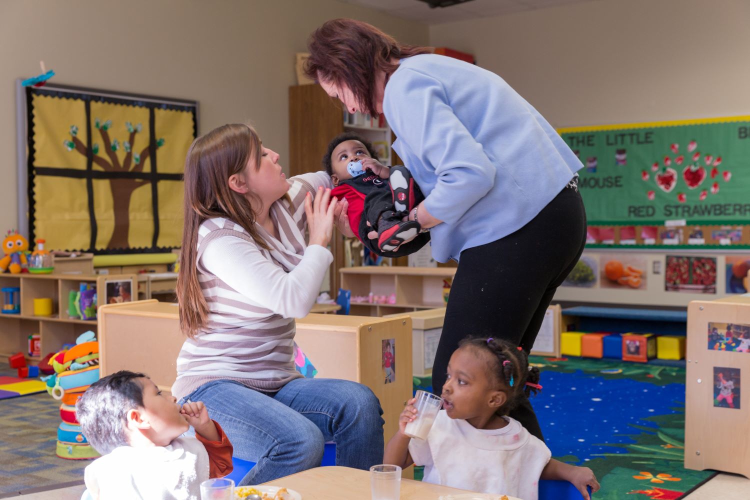 Maestra acunando y entregándole un niño pequeño a otra maestra.